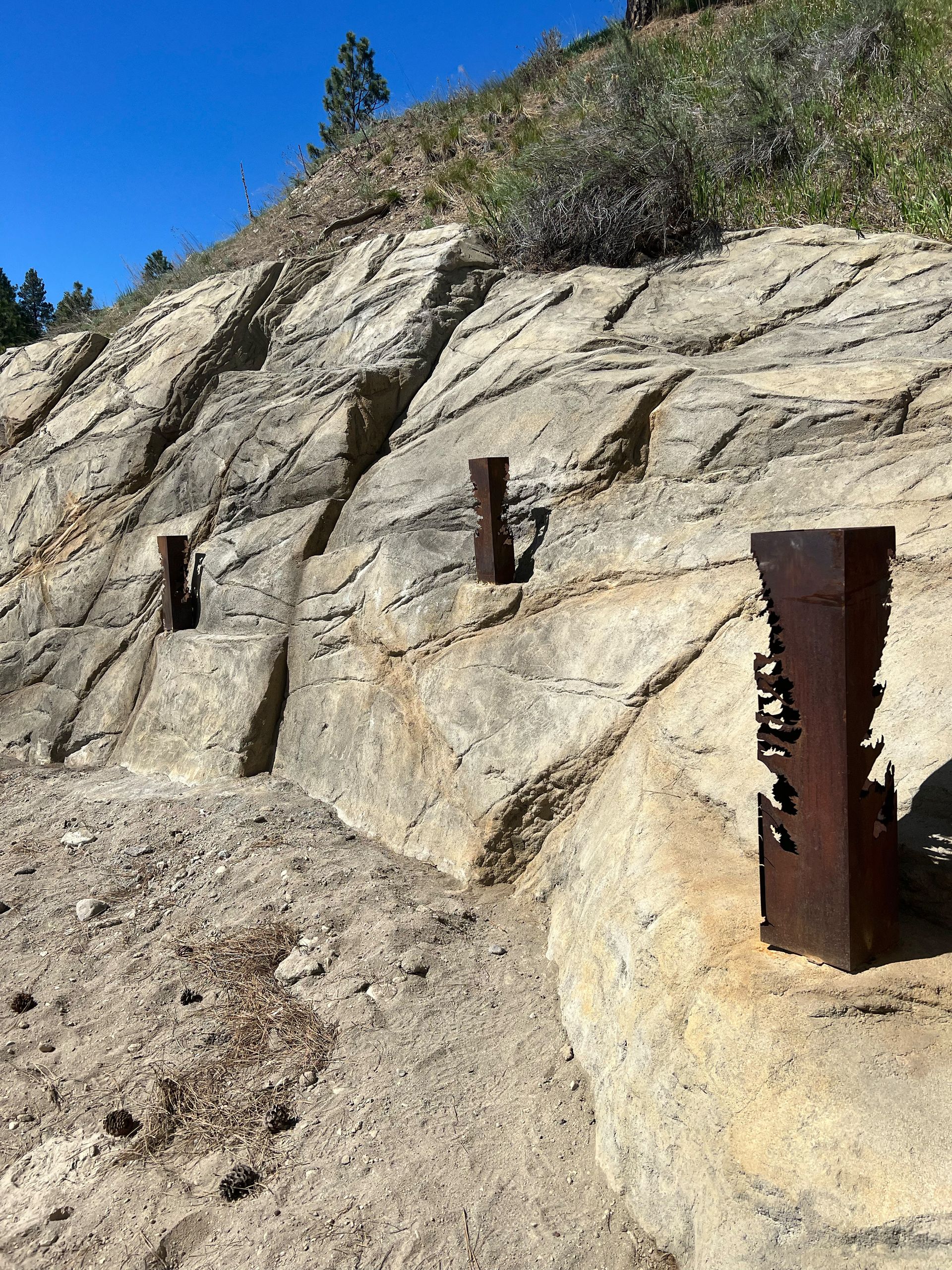Rocky hillside with rusted metal posts along a path.