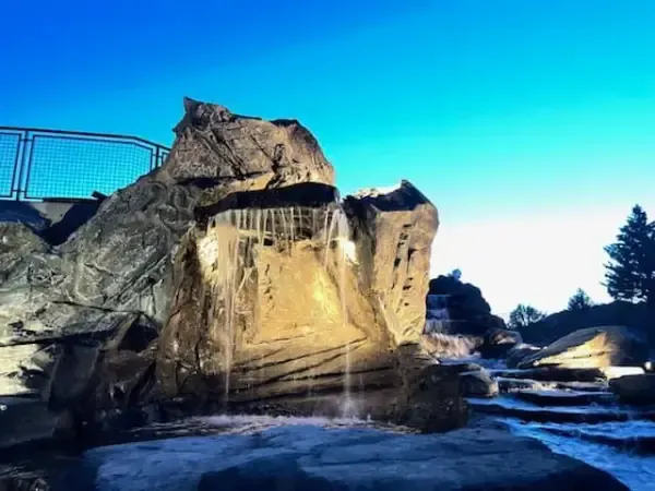 Artificial rock waterfall with water cascading down, set against a bright blue sky.