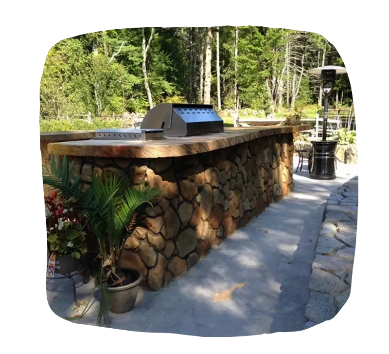 Outdoor kitchen with stone base, wooden countertop, grill, and potted plants.