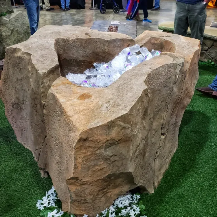 Large, carved rock cooler filled with ice, on green artificial turf.