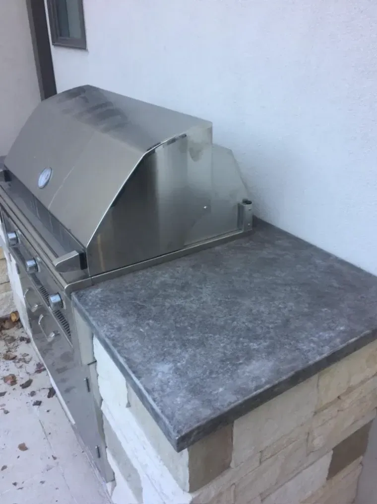 Stainless steel grill with a gray countertop built into a stone structure.