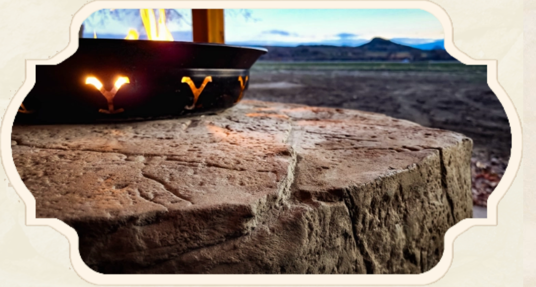 Fire pit with flames on a textured stone surface, mountains in the background.