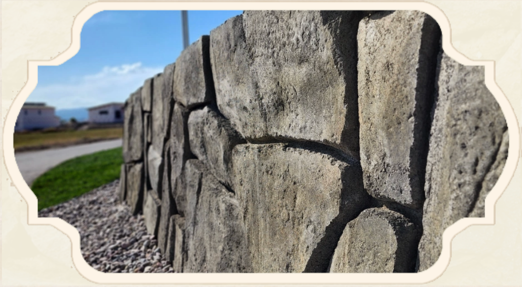 Close-up of a weathered stone wall with blue sky and grassy area in the background.