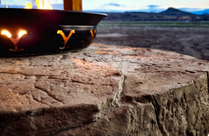 Fire pit with flames on a textured stone surface, mountains in the background.