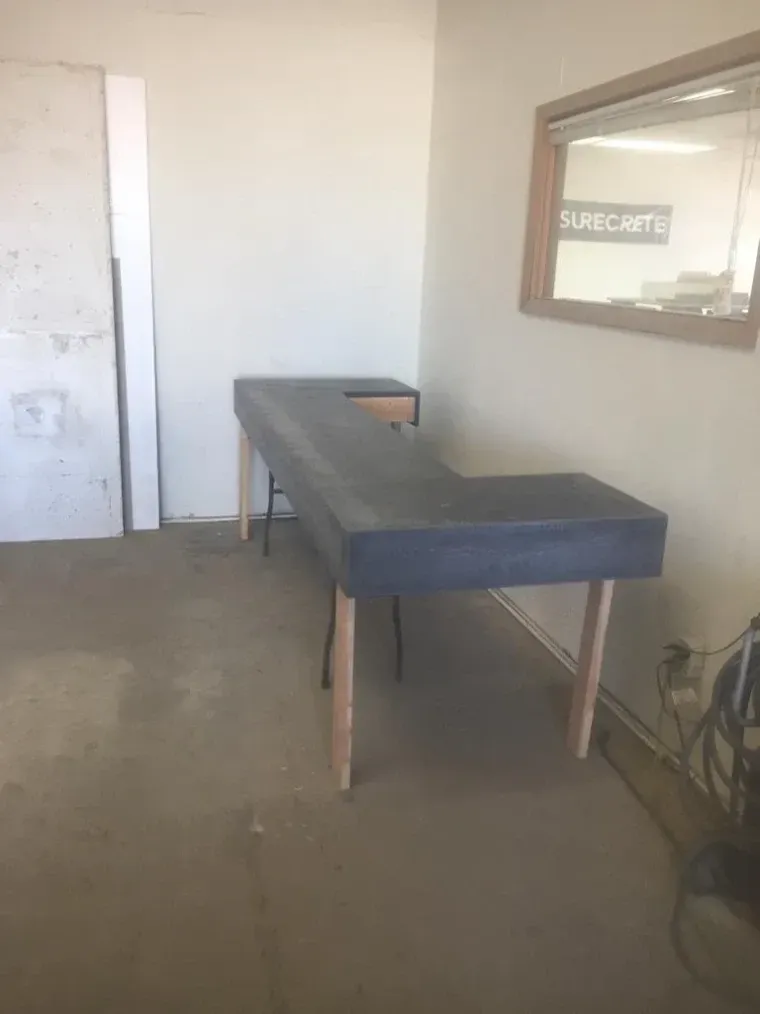 L-shaped desk with dark grey top and light wood legs in a room with a window and a door.