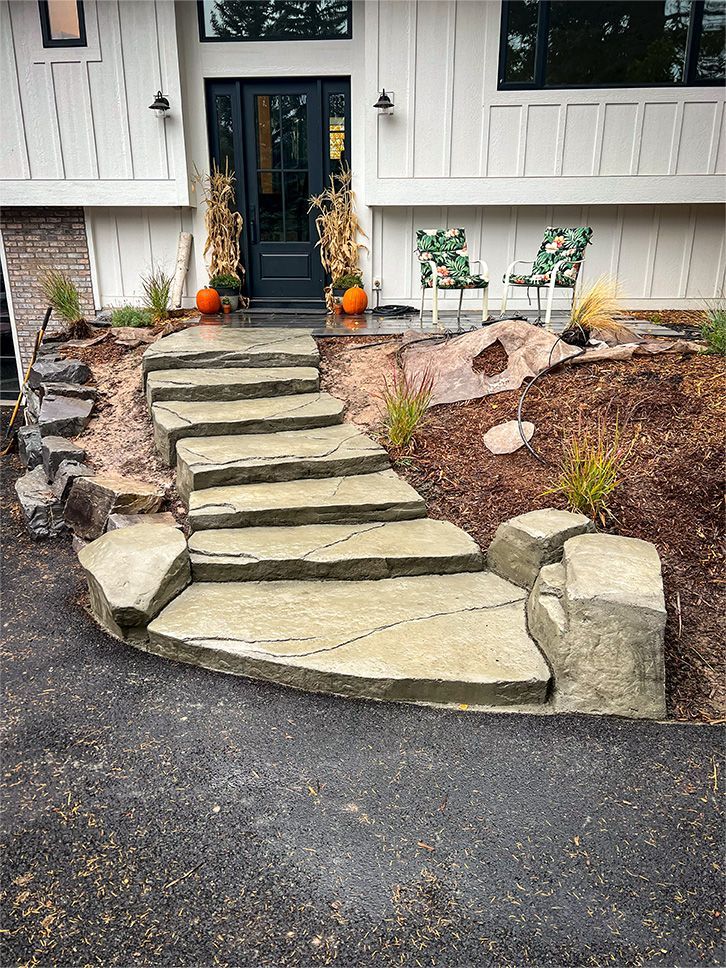 Stone steps lead up to a white house with a black door. Pumpkins and fall decor adorn the entrance.