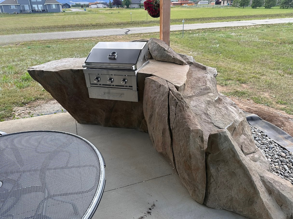 Outdoor grill built into a stone-covered island with food being cooked.