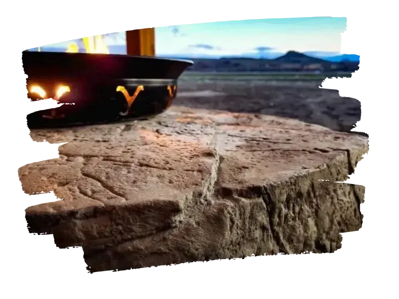 Fire pit with lit flames on a stone patio, mountain backdrop at dusk.