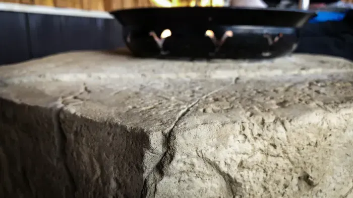Stone block supporting a black bowl with lit candle, warm glow.