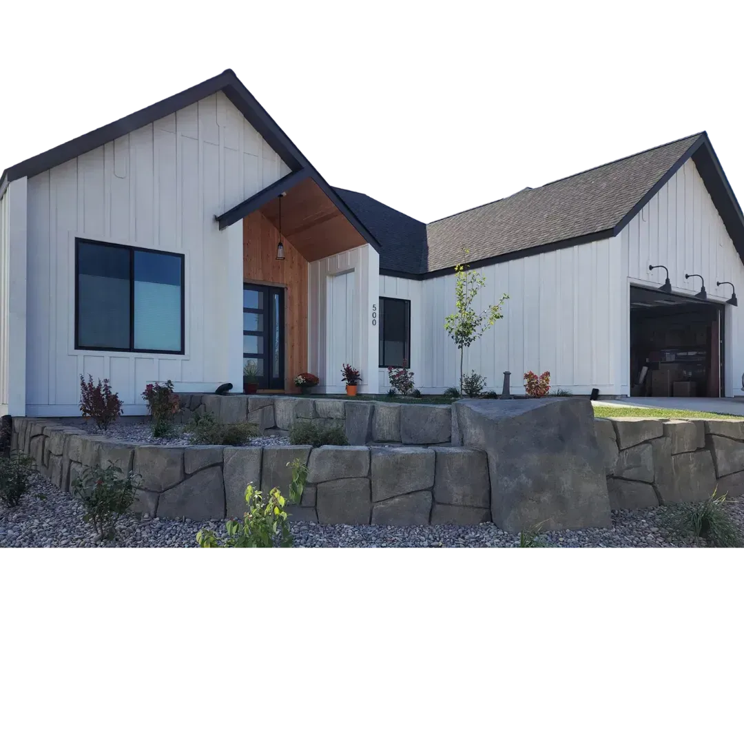 White farmhouse with black trim, a garage, and rock retaining wall.