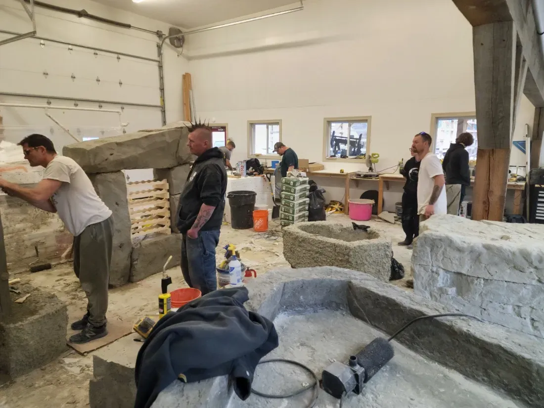 Workshop with several people working on large stone structures.