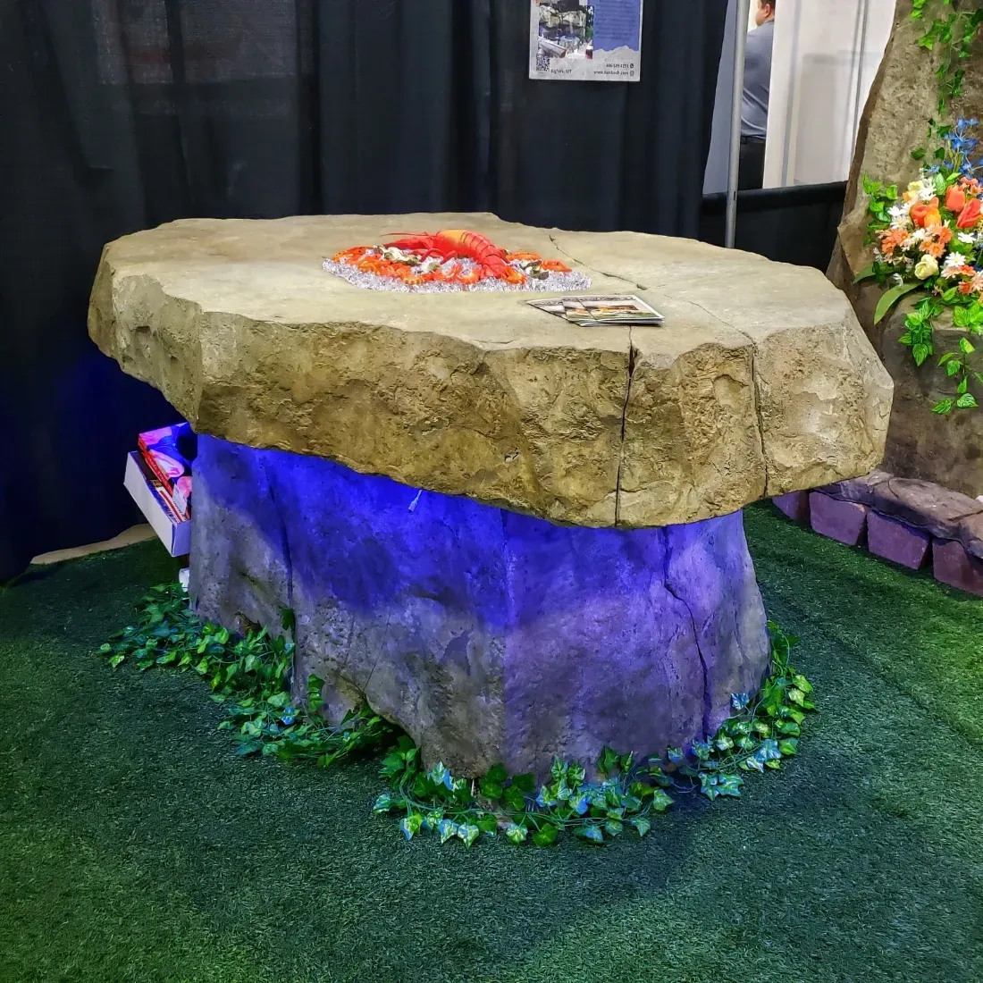 Stone fire pit table with blue underglow and decorative greenery on grass.