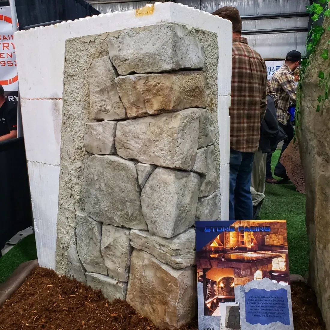 Display of a faux stone wall section at a trade show with onlookers.