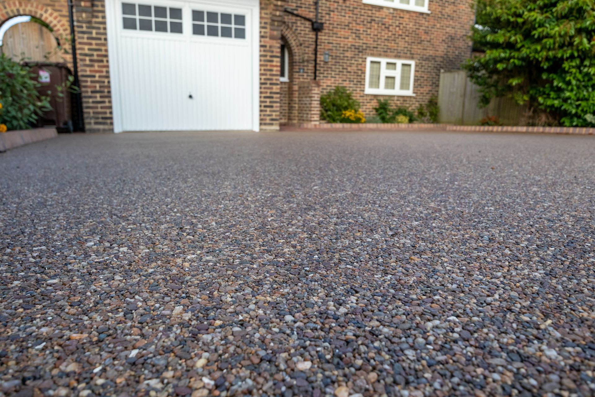 Close-up of a gravel driveway leading to a brick house with a white garage door.