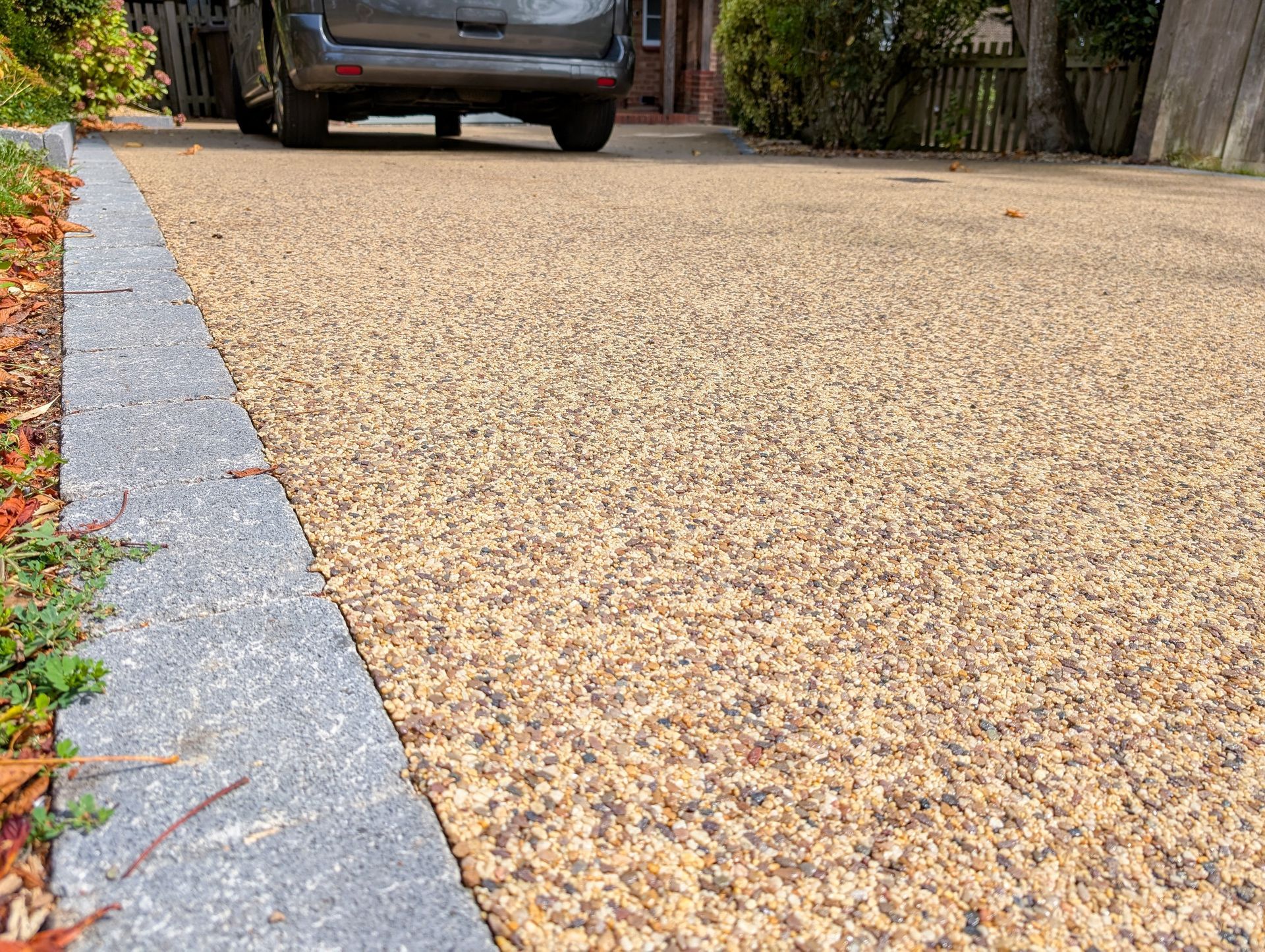 Driveway with tan resin-bound gravel next to a gray curb, a vehicle in the background.