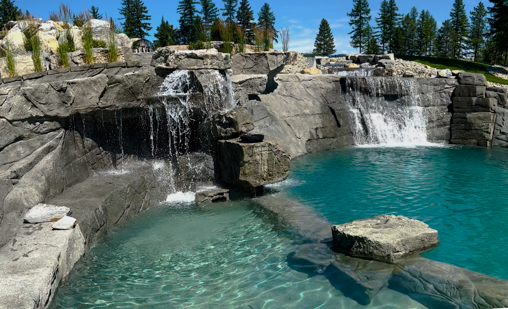 A large outdoor pool with waterfalls cascading over rocky formations; clear turquoise water.
