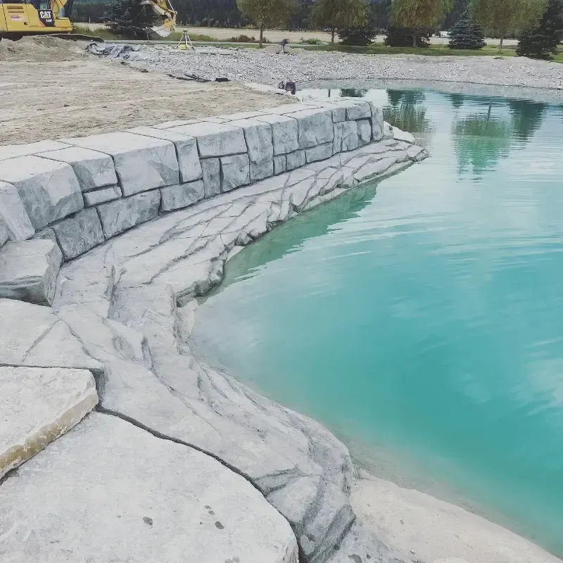 Artificial pond with decorative rock edging and retaining wall. Light blue water.