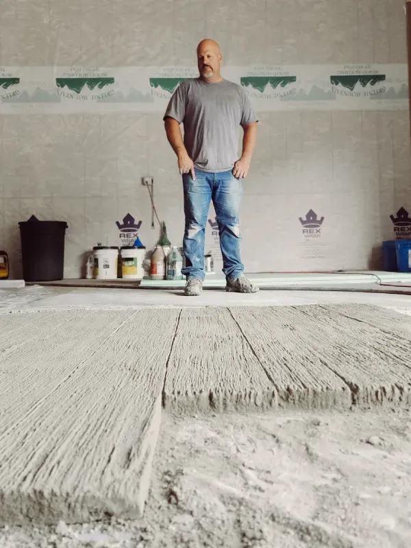Man in a gray shirt and jeans standing over textured concrete 