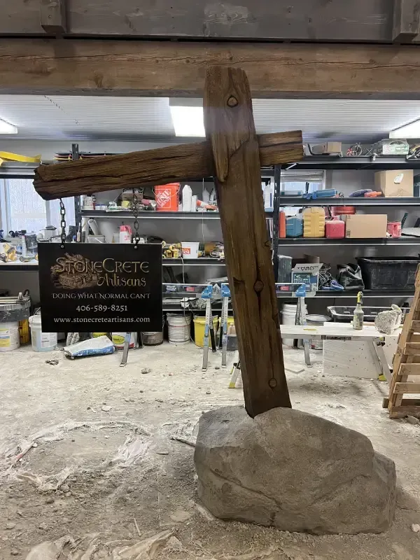 Wooden cross on large rock in workshop setting. Sign nearby.