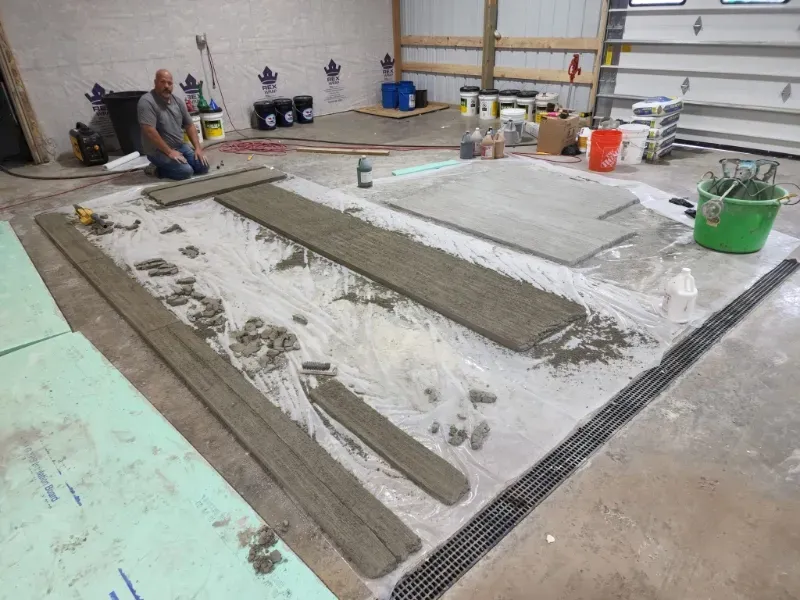 Man kneeling, applying cement to long wooden pieces inside a garage. Other wood and tools are nearby.