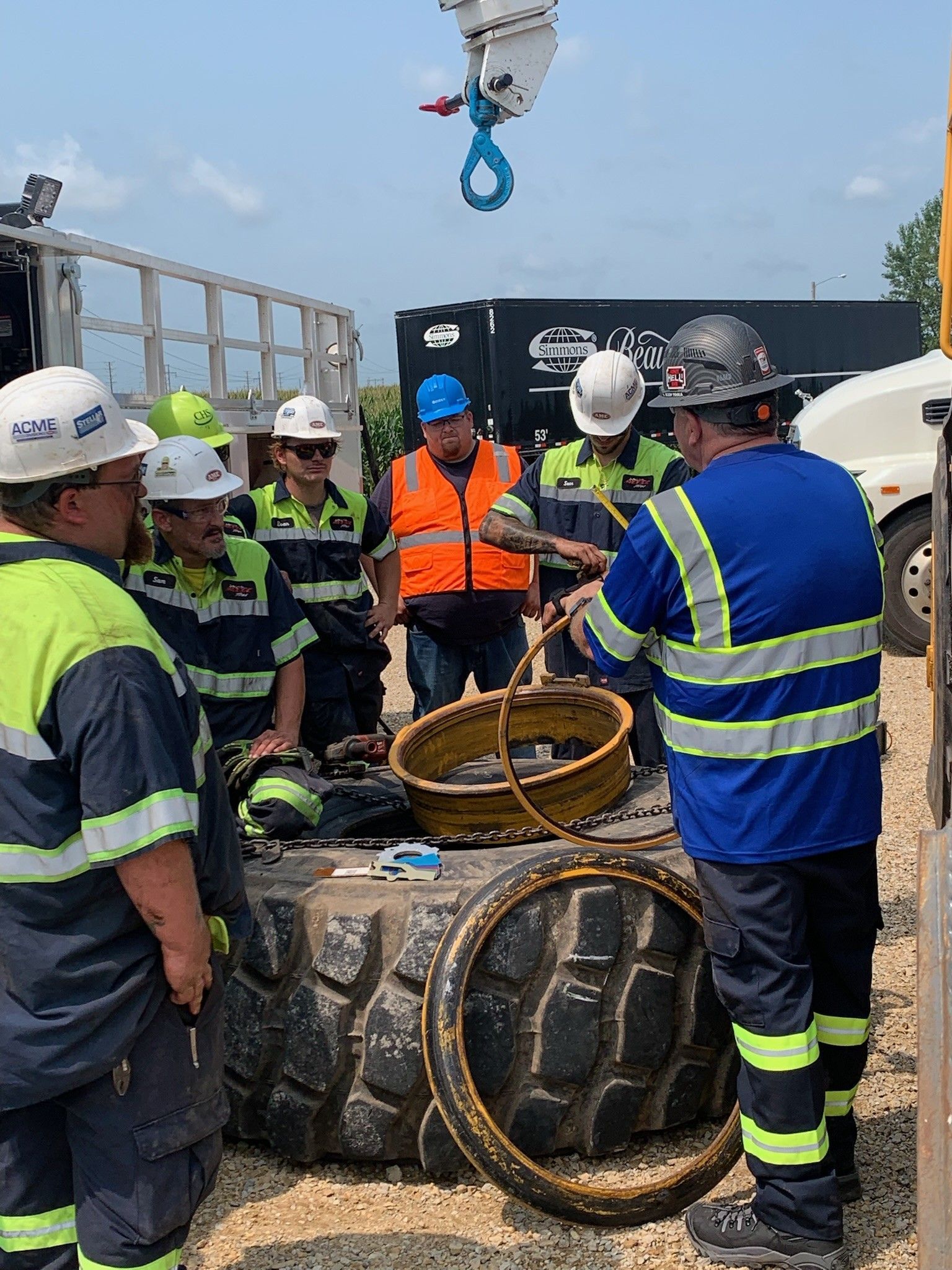 Group of workers in safety gear reviewing equipment near a large tire outdoors.