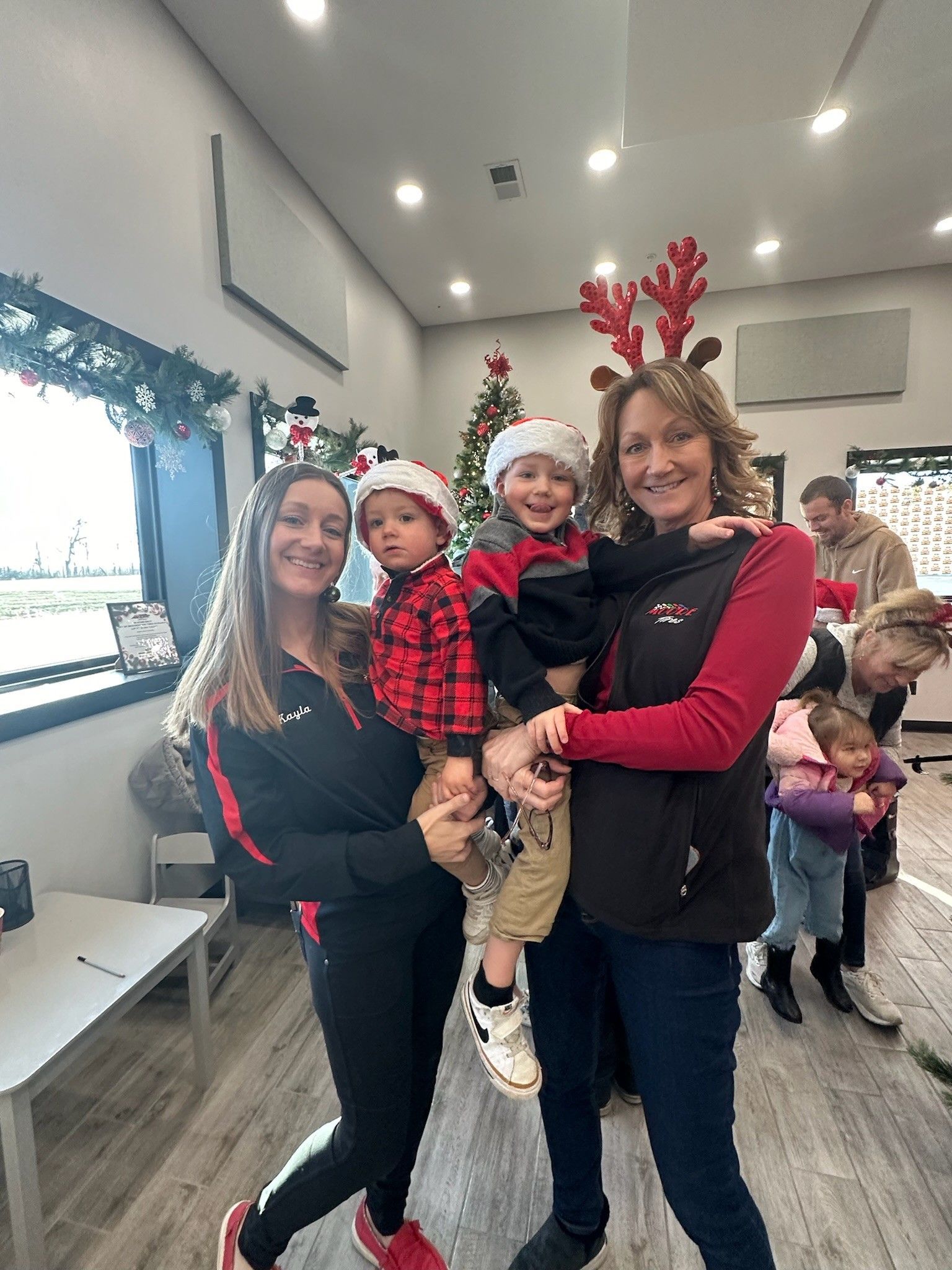 People in Christmas attire pose for photo, including two children, one with reindeer antlers. Indoors, festive decorations.