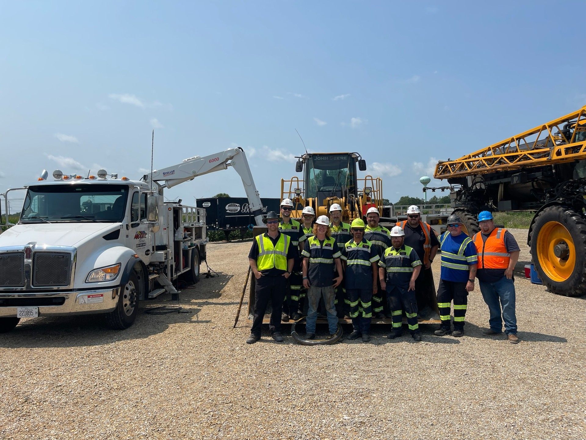 Group of workers in safety vests stand with heavy machinery on a sunny day.