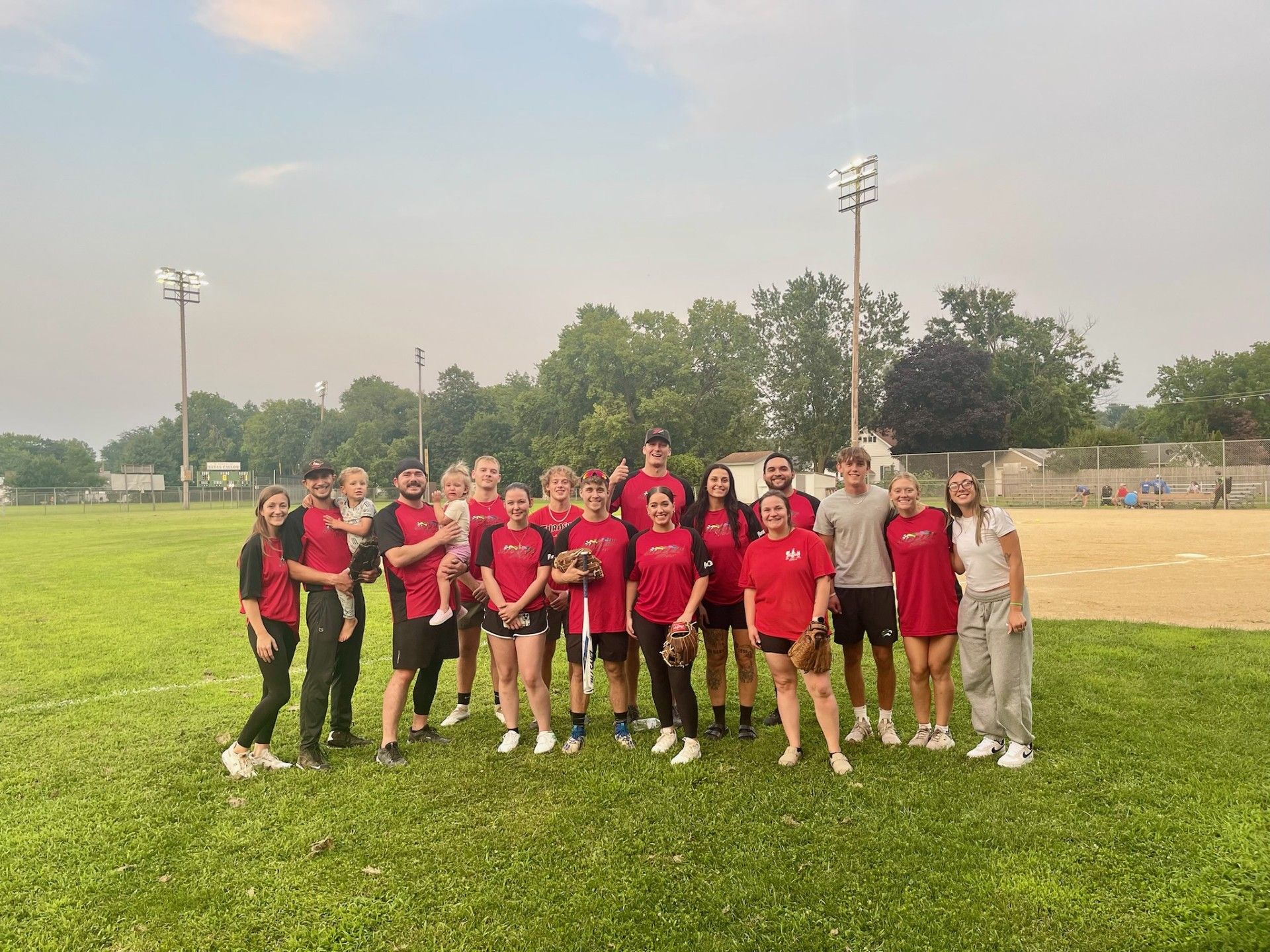 Softball team in red shirts and black and red sleeves posing on a baseball field.