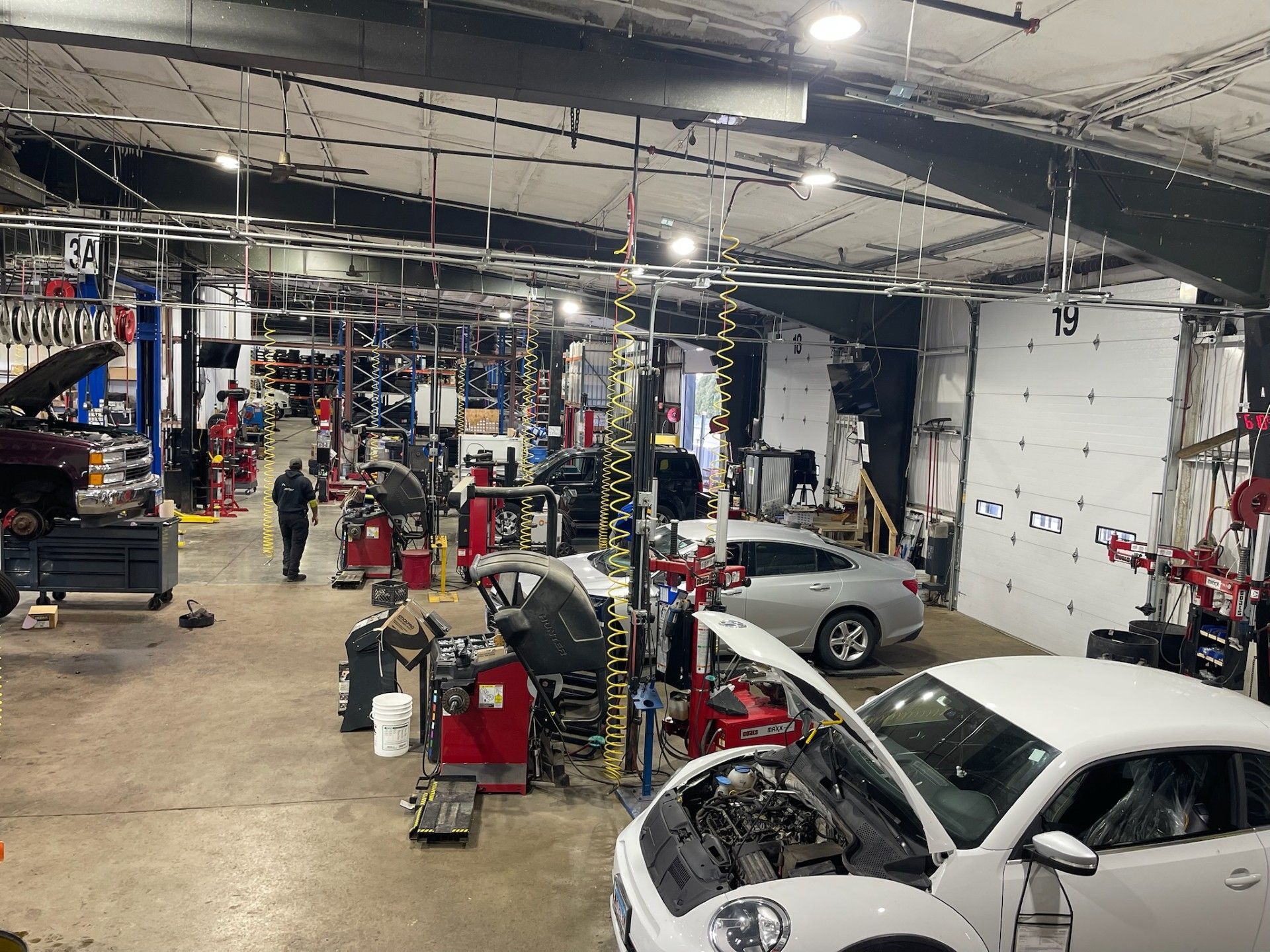 Inside a busy auto repair shop with multiple cars, tools, and a person walking.