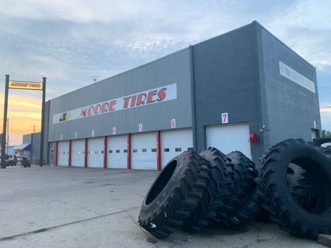 Moore Tires building with several garage doors and large tires in front.