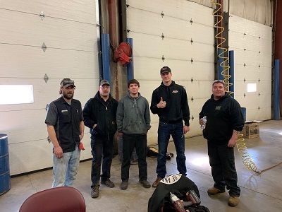 Five people standing in a garage, one giving a thumbs-up.