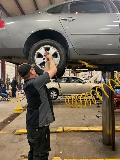 Mechanic working on a car raised on a lift in a garage. He is using a tool on a tire.