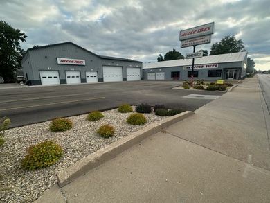 Two-building auto repair shop with business sign and landscaping along a street. Gray metal buildings.