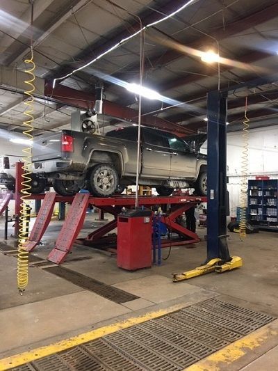 A truck on a red lift in an auto repair shop. The lift has ramps, and the shop is lit with overhead lights.