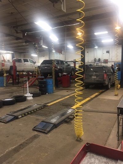 A car repair shop with vehicles on lifts, tools, and equipment. Bright lights and a yellow coil hose are visible.