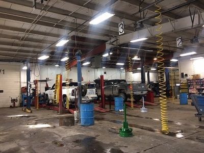 An auto repair shop with multiple vehicles on lifts. Concrete floor, overhead lights, and numbered service bays.