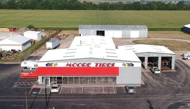 Moore Tires shop with red awning, multiple bays, and surrounding buildings in a rural setting.