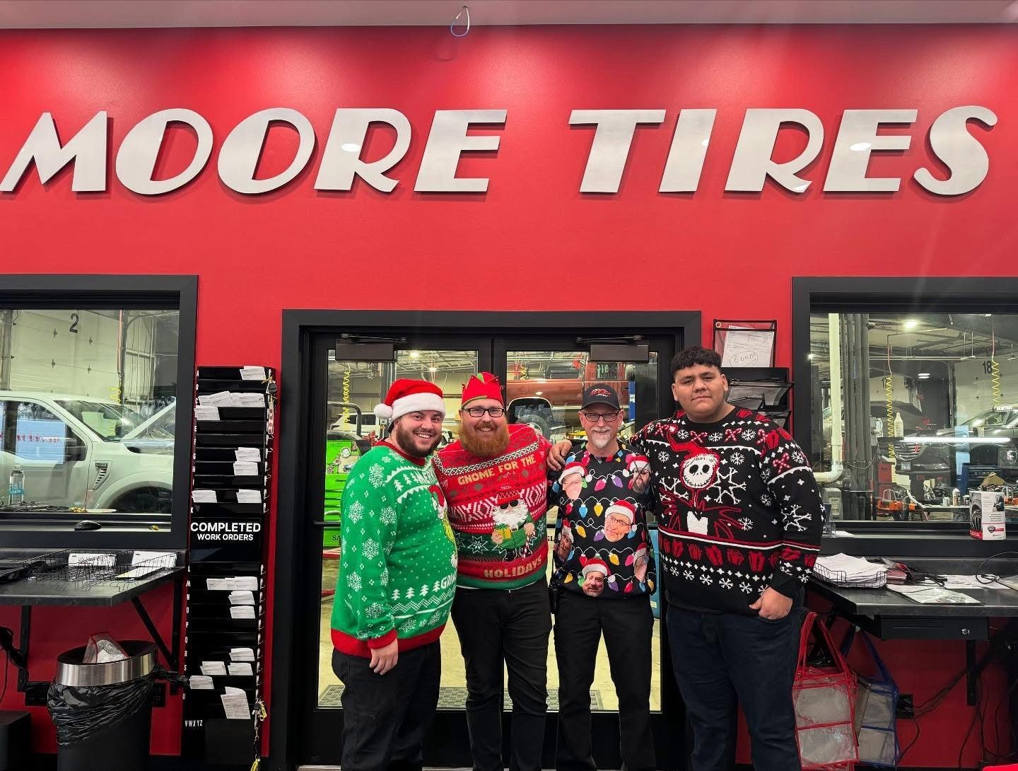 Four people in Christmas sweaters pose under a 