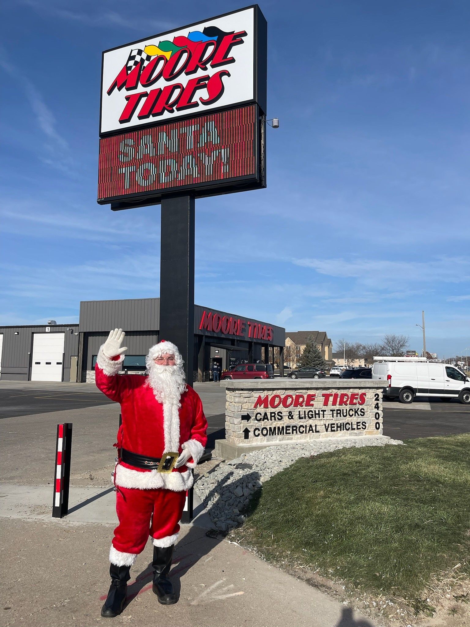 Santa Claus waves in front of Moody Tires sign.