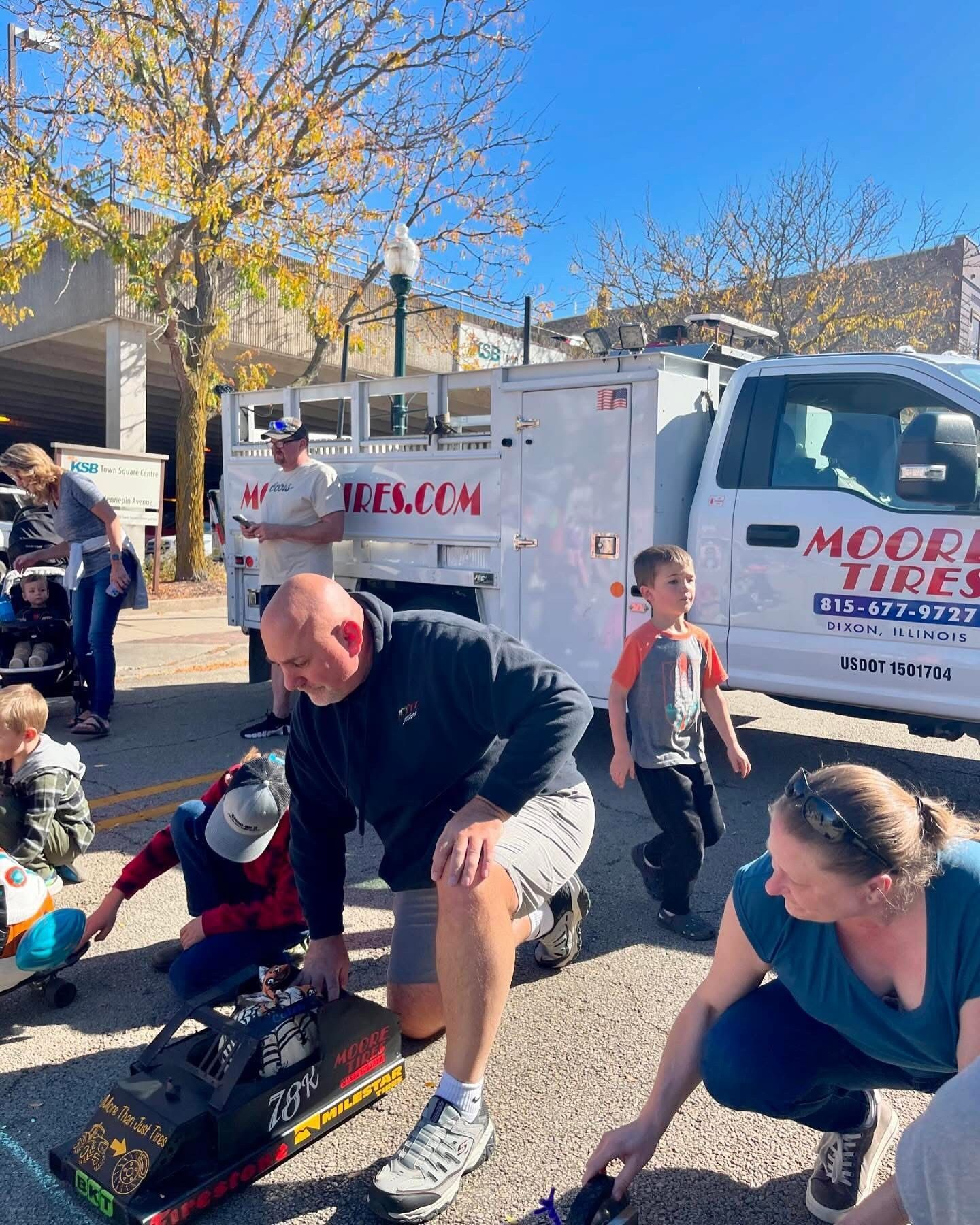 People picking up toy cars at an outdoor event near a truck with 