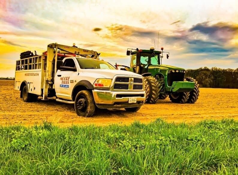White service truck and green tractor in a field at sunset.