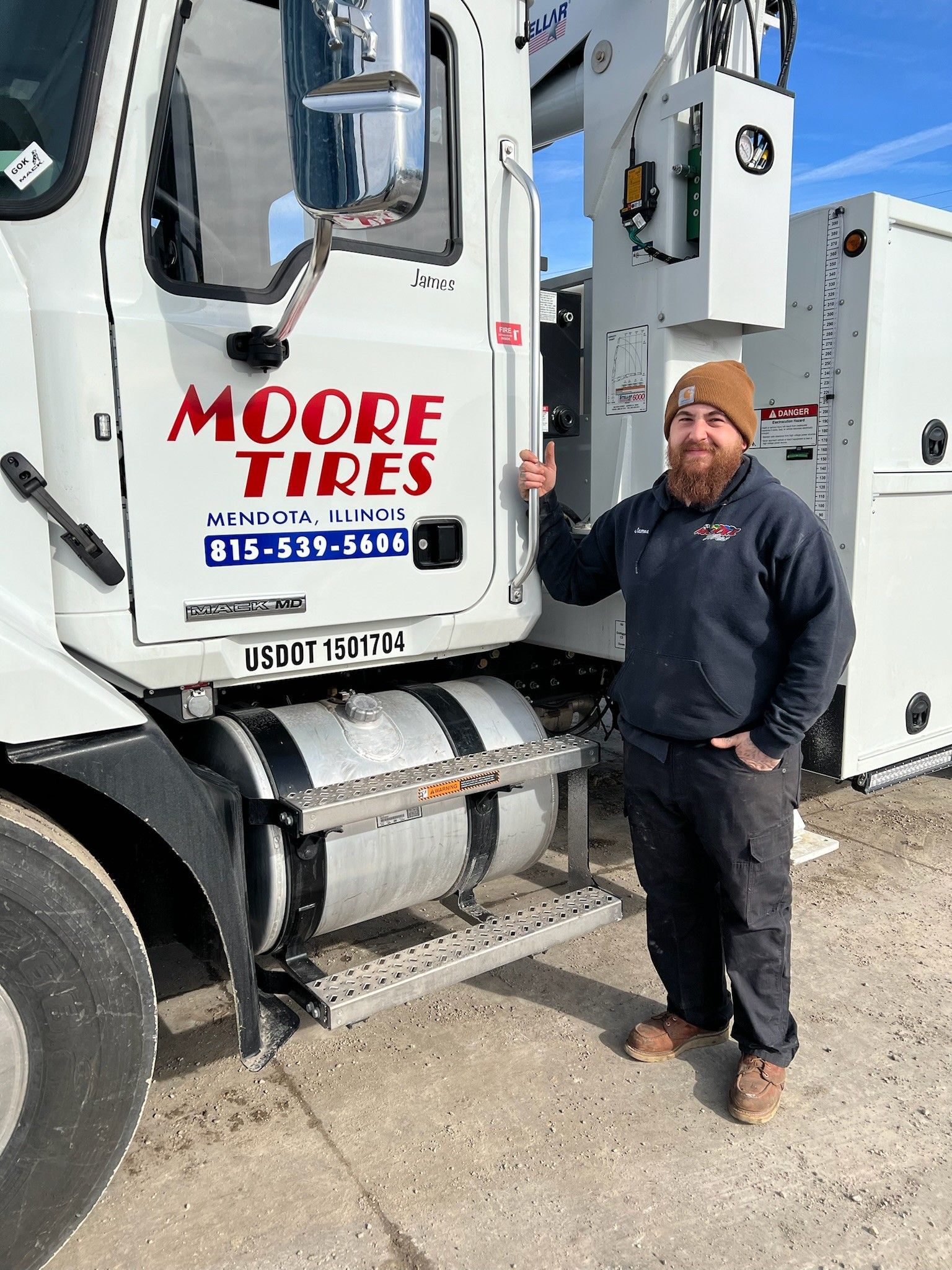 Man standing by a Moore Tires truck in front of a blue sky.