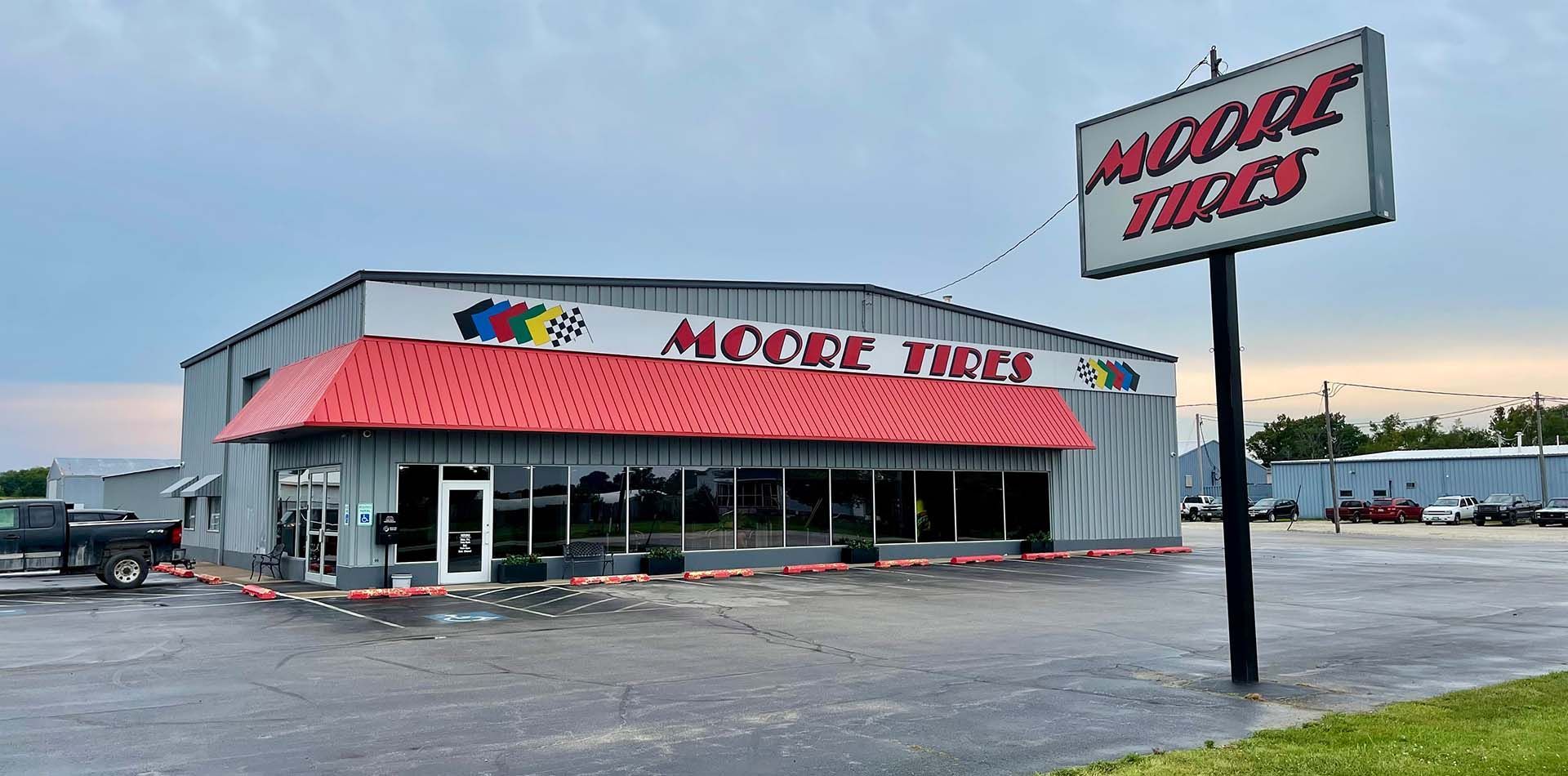 Moore Tires store building with red awning and sign in front of a gray sky.