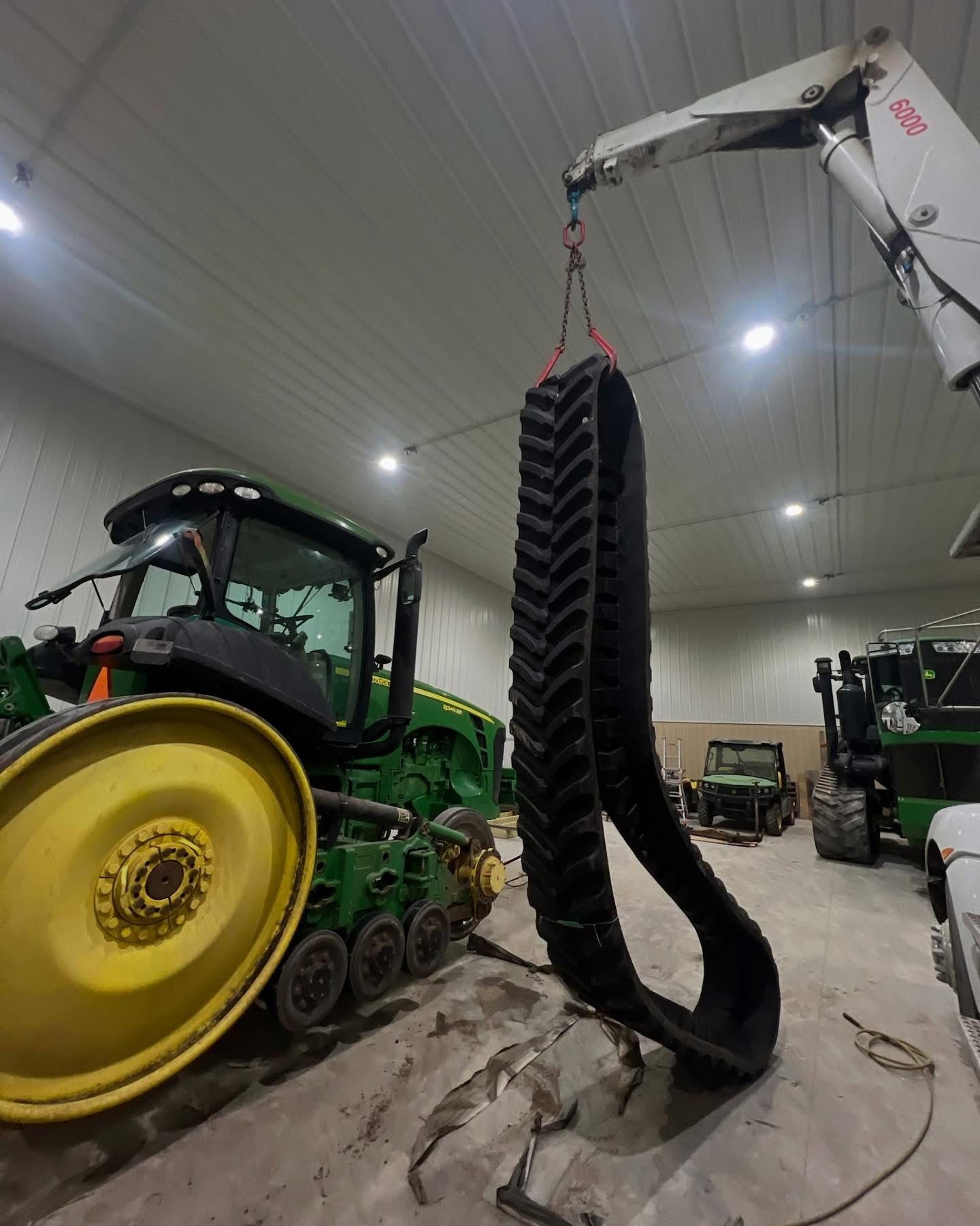 A tractor track being lifted by a crane inside a large building, near a green tractor.