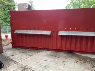 Red shipping container with multiple beer taps; outdoor setting.