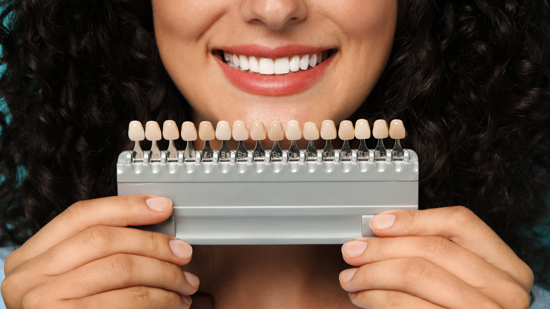 A woman is holding a tooth color chart in front of her mouth.