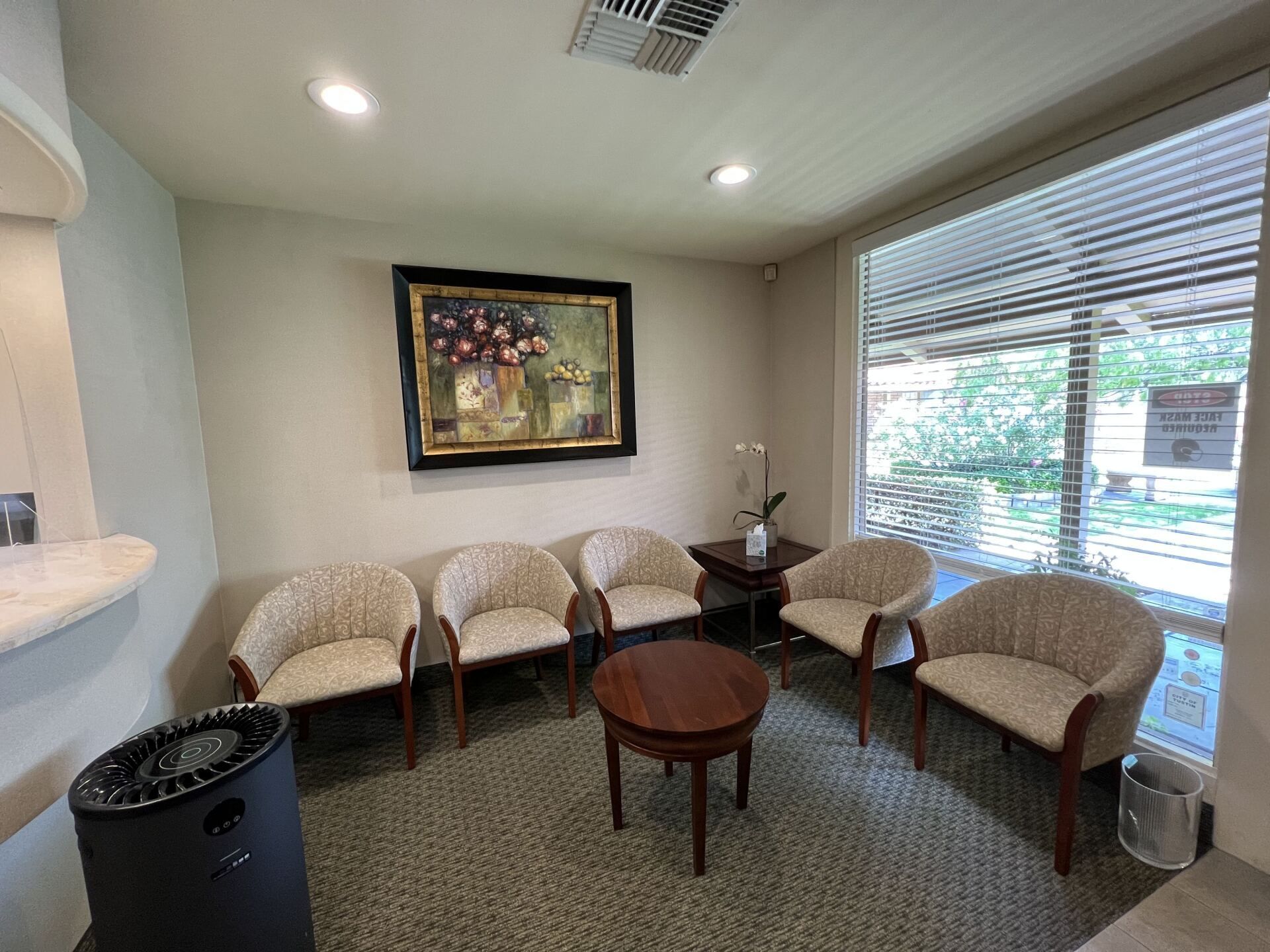 A waiting room with chairs , a table and a painting on the wall.