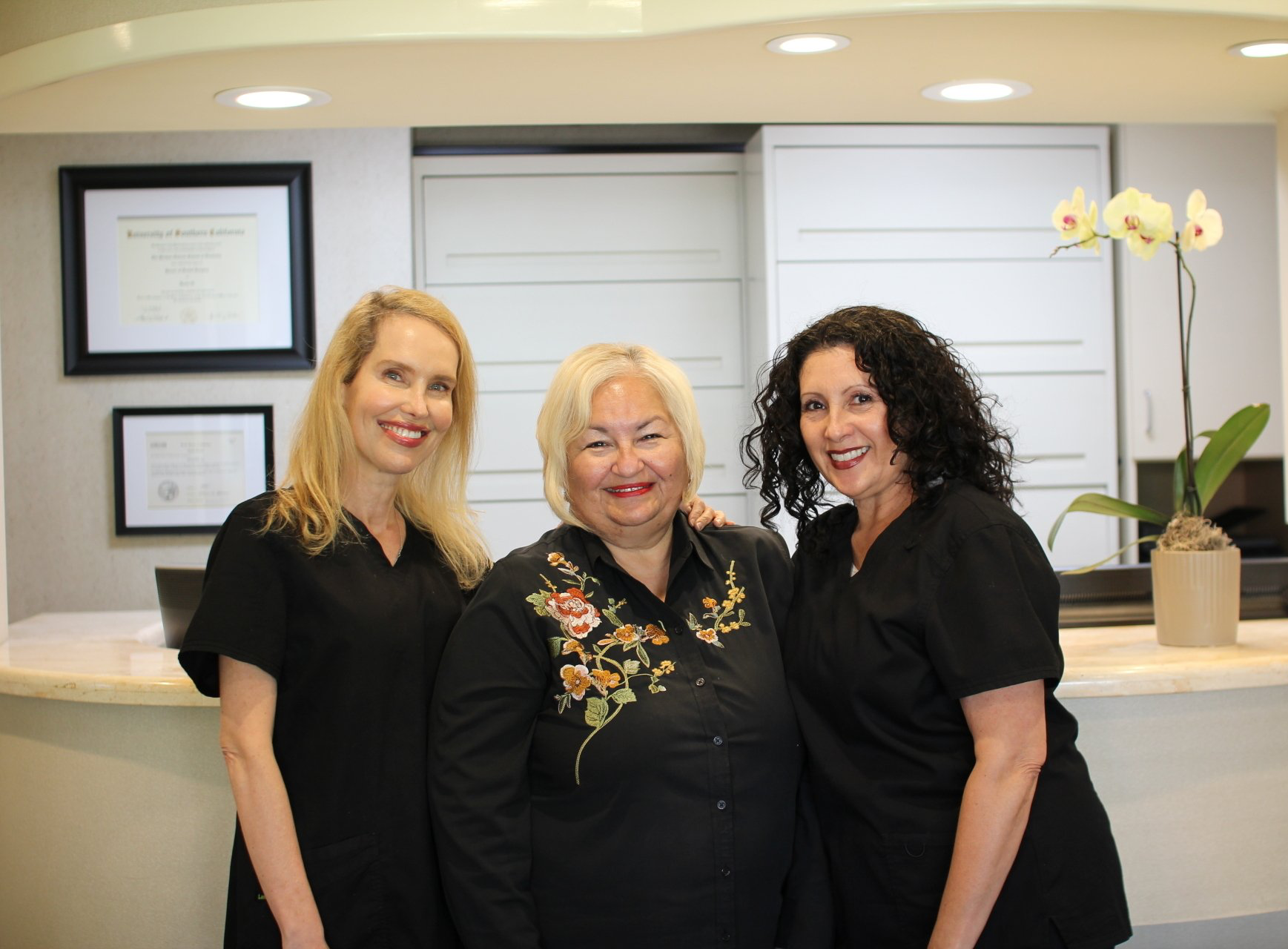 Three women are posing for a picture in a dental office.
