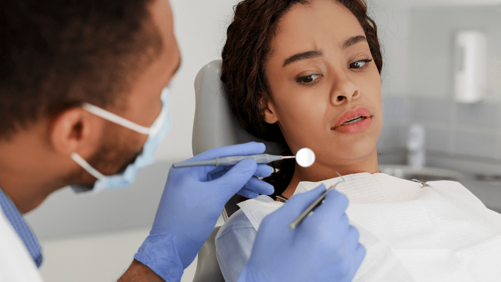 A woman is sitting in a dental chair while a dentist examines her teeth.
