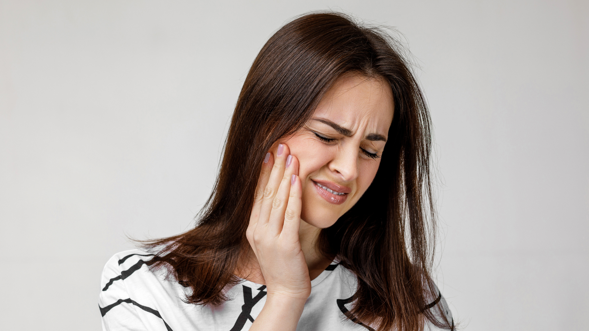 Woman grimacing and holding her cheek against a plain background